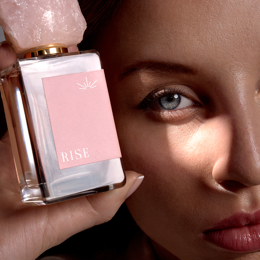 RISE eau de parfum held in hand, rose quartz cap in the light